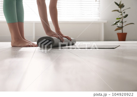 Woman rolling her mat on floor in yoga studio, closeup 104920922