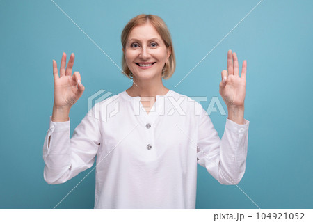 happy blonde 50s woman in white blouse in menopause on studio background 104921052