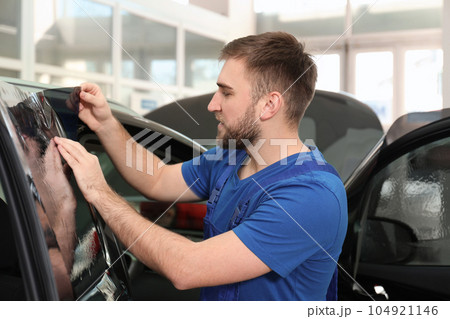Worker tinting car window with foil in workshop Worker tinting car window with foil in workshop 104921146