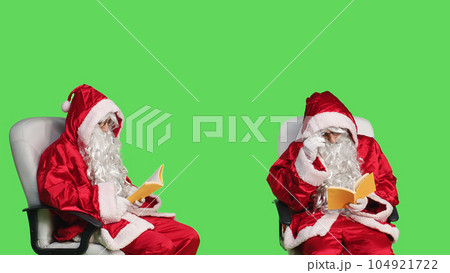 Santa claus reading fiction book in studio, enjoying literature or poetry lecture for knowledge. Saint nick sitting on chair with fairytale story in hand, greenscreen backdrop. Santa claus reading fiction book in studio, enjoying literature or poetry lecture for knowledge. Saint nick sitting on chair with fairytale story in hand, greenscreen backdrop. 104921722