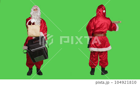 Deliveryman in red santa suit carrying backpack with pizza box and paper bag order, christmas eve delivery concept. Young man saint nick character against full body greenscreen backdrop. 104921810