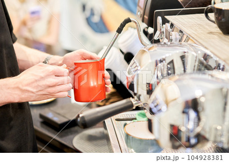Barista pours cream into the cup of coffee. A small coffee business. A professional barista prepares coffee in a carob coffee machine. Favorite job in the restaurant industry. Barista pours cream into the cup of coffee. A small coffee business. A professional barista prepares coffee in a carob coffee machine. Favorite job in the restaurant industry. 104928381