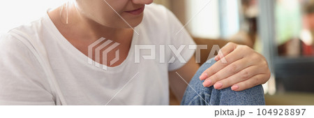 Woman sits at home and feels pain in her knee. 104928897