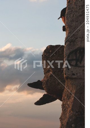Vertical shot of a guy in a cap sitting on a stone surface admiring the sky 104931475