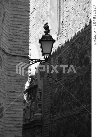 Vertical black and white shot of a dove perching on a lantern in the old town of Toledo, Spain Vertical black and white shot of a dove perching on a lantern in the old town of Toledo, Spain 104931527