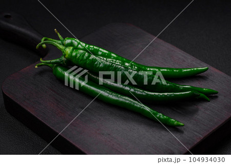 Fresh hot green chili peppers on a dark concrete background Fresh hot green chili peppers on a dark concrete background 104934030