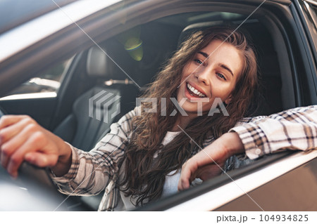 Portrait of a beautiful smiling woman in a car looking out of the window 104934825