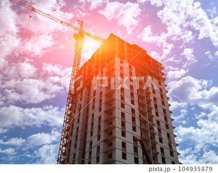 Construction crane is building a multi-storey house, in summer against the blue sky. Construction crane is building a multi-storey house, in summer against the blue sky. 104935879