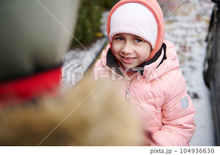 Caucasian lovely little child girl smiling looking at camera, standing near her older brother in a snow covered backyard Caucasian lovely little child girl smiling looking at camera, standing near her older brother in a snow covered backyard 104936630