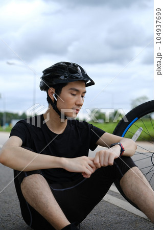 Young sportsman taking a break after riding bicycle and checking sport activity progress data on smartwatch Young sportsman taking a break after riding bicycle and checking sport activity progress data on smartwatch 104937699