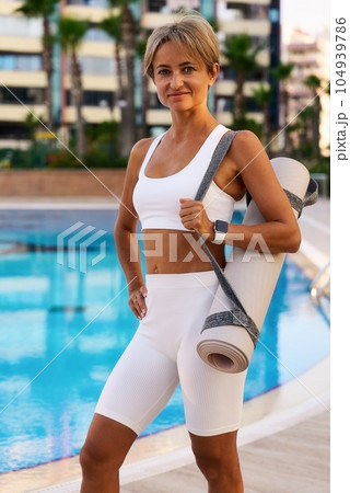 Portrait of young slim and healthy caucasian girl doing workout in park, standing with water bottle 104939786