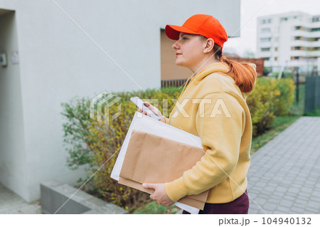 Happy Delivery woman with smartphone and parcel in hands front of the house. Courier send a package to destination. Happy professional shipping courier. Delivery postal service. Happy Delivery woman with smartphone and parcel in hands front of the house. Courier send a package to destination. Happy professional shipping courier. Delivery postal service. 104940132