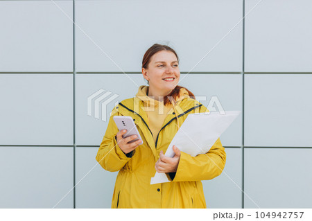 Young woman in yellow uniform using smartphone and holding package. Delivery service holding to sent a white package letter, for mockup Young woman in yellow uniform using smartphone and holding package. Delivery service holding to sent a white package letter, for mockup 104942757