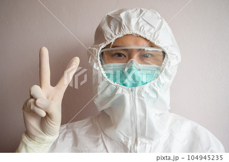 Nurse wearing PPE suit with mask for protect virus and showing victory. In coronavirus pandemic outbreak we should support and encourage healthcare worker by stay home and listen to medical advice. Nurse wearing PPE suit with mask for protect virus and showing victory. In coronavirus pandemic outbreak we should support and encourage healthcare worker by stay home and listen to medical advice. 104945235