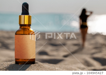 Natural sun protection concept. Dropper bottle on the beach. Blurred silhouette of a woman, the concept of skin protection. Natural sun protection concept. Dropper bottle on the beach. Blurred silhouette of a woman, the concept of skin protection. 104945427