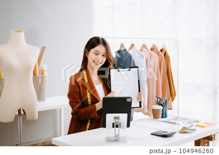 Asian tailor woman working on clothes in tailoring atelier. beautiful young female fashion designer smile and after success in studio.. Asian tailor woman working on clothes in tailoring atelier. beautiful young female fashion designer smile and after success in studio.. 104946260