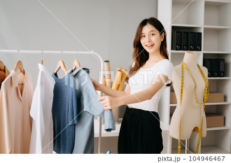 Asian tailor woman working on clothes in tailoring atelier.  beautiful young female fashion designer smile and after success in modern studio 104946467