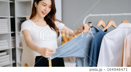 Asian young woman on desk in office of fashion designer and holds tablet, laptop and smartphone on white table Asian young woman on desk in office of fashion designer and holds tablet, laptop and smartphone on white table 104946471