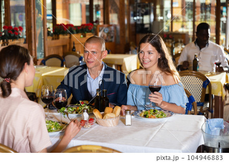 Company of smiling friends having dinner in restaurant 104946883