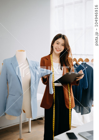Fashion designer woman talking smart phone and using laptop with digital tablet computer in modern studio the clothes hanging on the racks morning light Fashion designer woman talking smart phone and using laptop with digital tablet computer in modern studio the clothes hanging on the racks morning light 104946916