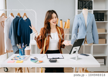 Fashion designer woman talking smart phone and using laptop with digital tablet computer in modern studio the clothes hanging on the racks morning light Fashion designer woman talking smart phone and using laptop with digital tablet computer in modern studio the clothes hanging on the racks morning light 104946918