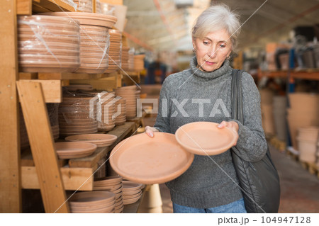 Eldrely woman selecting earthenware crockery in shop 104947128
