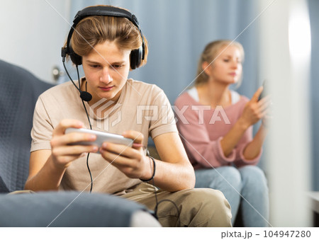 Excited teen boy playing online game on cell phone at home Excited teen boy playing online game on cell phone at home 104947280