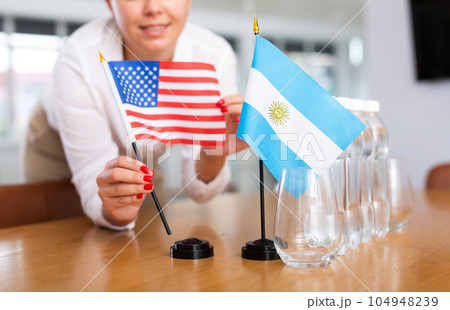 Unrecognizable girl sets midget flags of Argentina and USA before international negotiations 104948239