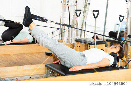 Young Hispanic woman performing pilates on reformer in fitness studio 104948604