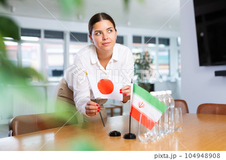 Positive young woman putting little flag of Japan on table next to the flag of Iran 104948908