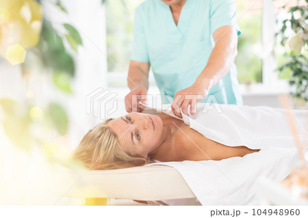 Male therapist covers woman client with white terry sheet after relaxing massage procedure 104948960