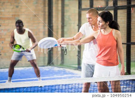 Man teaching woman to hold paddle racquet on indoor court Man teaching woman to hold paddle racquet on indoor court 104950254
