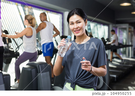 Woman standing with drinking water in gym Woman standing with drinking water in gym 104950255