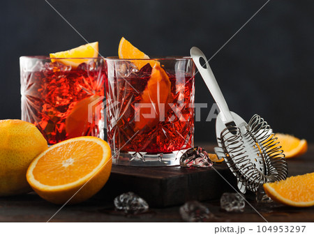 Negroni cocktail in crystal glasses with orange slice and fresh raw oranges  104953297