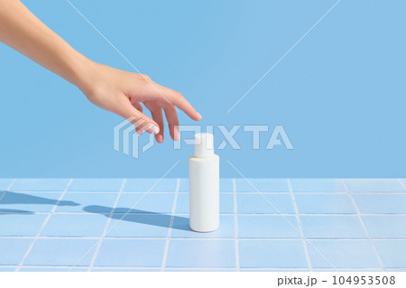 Womans hand holding white tube on blue tile background. Beauty treatment. Skin care routine Womans hand holding white tube on blue tile background. Beauty treatment. Skin care routine 104953508