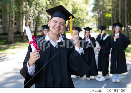 Happy young caucasian man celebrating graduation. Crowd of students graduates outdoors. 104954064