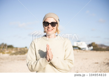 Portrait of young stylish woman wearing wool sweater, wool cap and sunglasses on long sandy beach in spring. 104954810