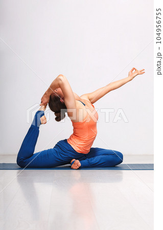 Woman doing Hatha yoga asana Eka pada rajakapotasana - one-legged king pigeon pose on yoga mat on yoga mat in studio on grey bagckground 104956755