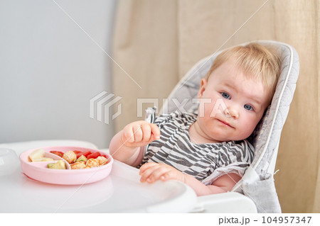 Cute child eats healthy food vegetables and meatballs from dietary meat steamed,. Portraits of a cute 10 months old baby girl. The baby sitting in a special high chair for babies. 104957347