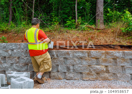 On construction site construction worker was mounting concrete blocks to retaining wall On construction site construction worker was mounting concrete blocks to retaining wall 104958657