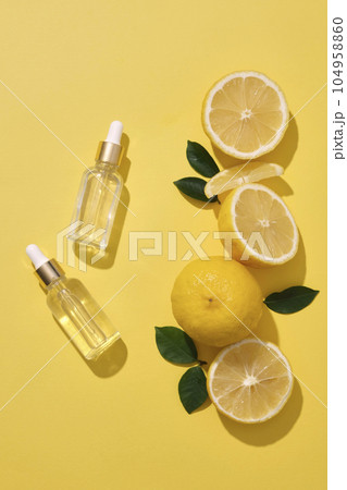 Lemon cut in halves and slices are arranged with two empty label glass dropper bottle against yellow background. Natural beauty product mockup design 104958860