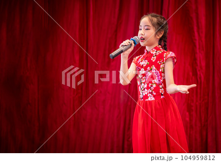 The Asian kid girl sing a song on stage at her school activity day, dress in Qipao style, red curtain background 104959812