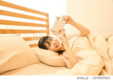 ベッドでスマホを使う女性 104960002
