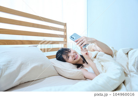ベッドでスマホを使う女性 ベッドでスマホを使う女性 104960016
