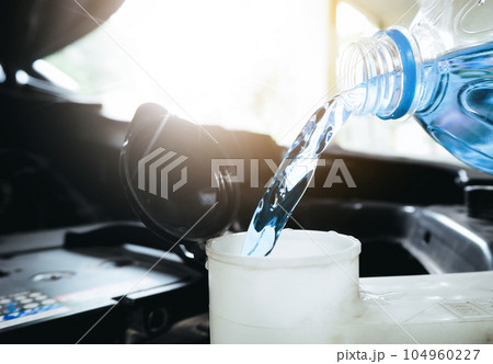Close up of a bottle of water being poured into a windshield washer tank. Close up of a bottle of water being poured into a windshield washer tank. 104960227