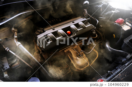 Closeup of a broken car engine with smoke coming out of the engine compartment. Closeup of a broken car engine with smoke coming out of the engine compartment. 104960229