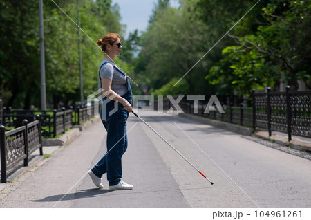 Blind pregnant woman crosses the street with the help of a tactile cane. Blind pregnant woman crosses the street with the help of a tactile cane. 104961261