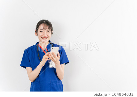 スマホを持った青いクリニックユニフォームの医療従事者の女性(医者・医師) スマホを持った青いクリニックユニフォームの医療従事者の女性(医者・医師) 104964633