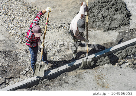 Roadway repair. Two handymen laying curbs on road on summer day. Restoration of road surface 104966652