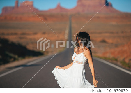 Happy young woman in white dress on the famous road to Monument Valley in Utah. Amazing view of the Monument valley. Happy young woman in white dress on the famous road to Monument Valley in Utah. Amazing view of the Monument valley. 104970879